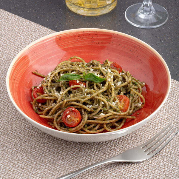 A round, deep porcelain plate with a red and white two-tone design, filled with spaghetti pasta and garnished with cherry tomatoes and basil.