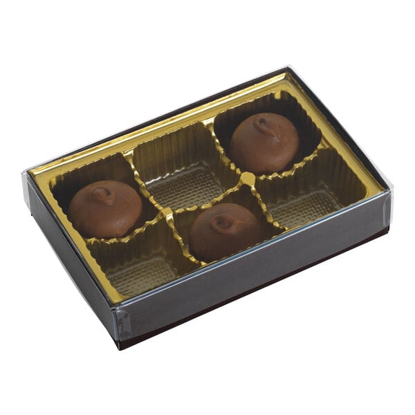 A small rectangular brown and gold candy box with a transparent lid, containing three pieces of chocolate in a six-cavity tray.