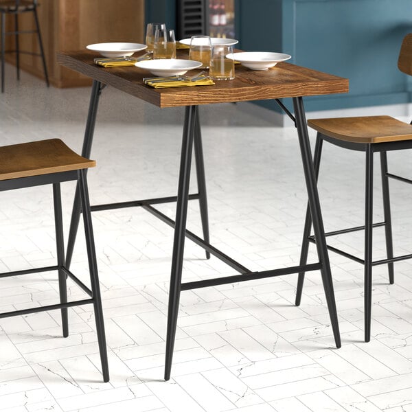 A rectangular bar height table with a wooden top and black metal legs, set for dining.