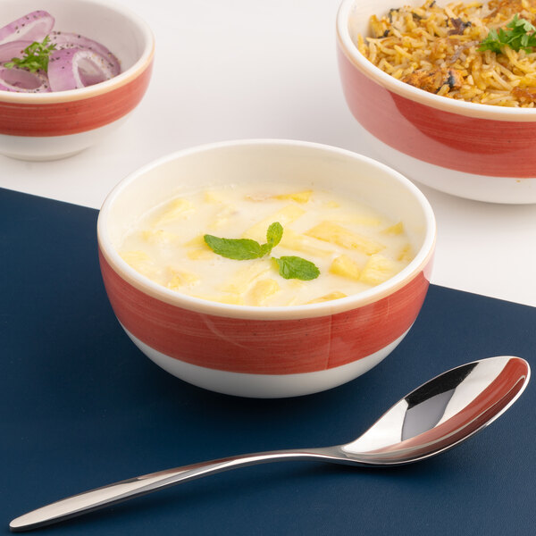 A red and white two-tone round porcelain bowl filled with a creamy dish, garnished with mint leaves.