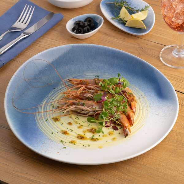 A blue and white ombre slanted porcelain flat coupe plate with shrimp and garnish served on it.