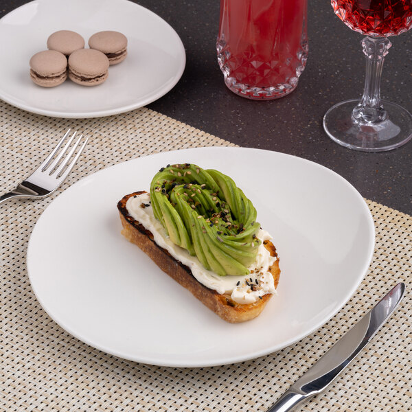 A round, warm white porcelain coupe plate with a slanted edge, shown holding avocado toast.