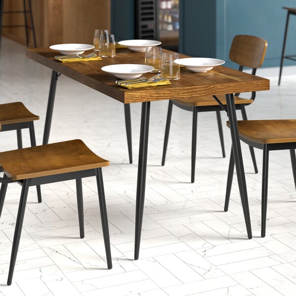 A rectangular mid-century style dining table with a wooden top and black metal legs, set with plates, glasses, and utensils.