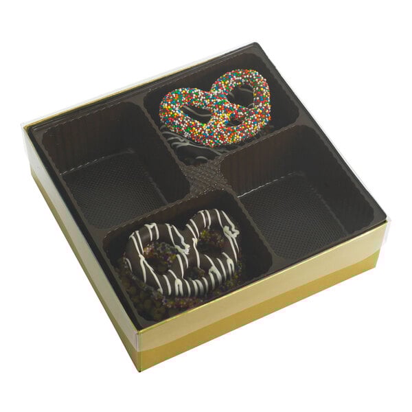 A gold and brown candy box with four cavities, containing two chocolate-covered pretzels and a transparent lid.