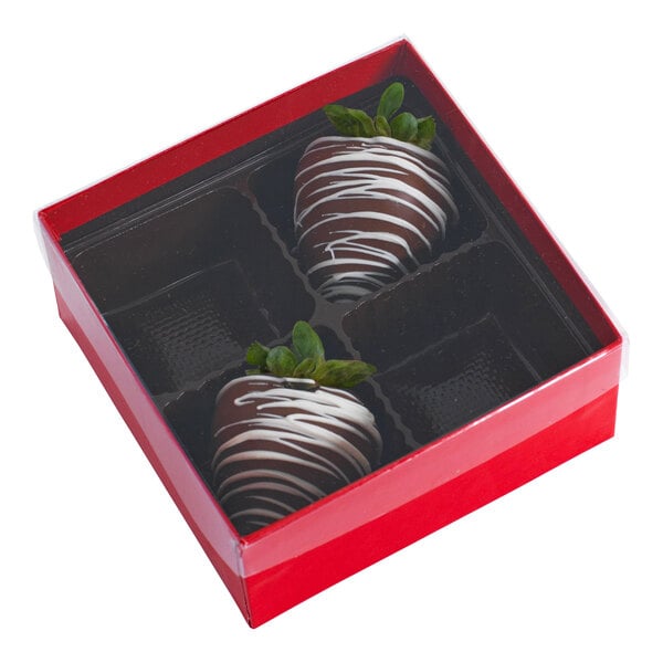 A red and black candy box with a transparent lid containing two chocolate-covered strawberries in a four-cavity insert.
