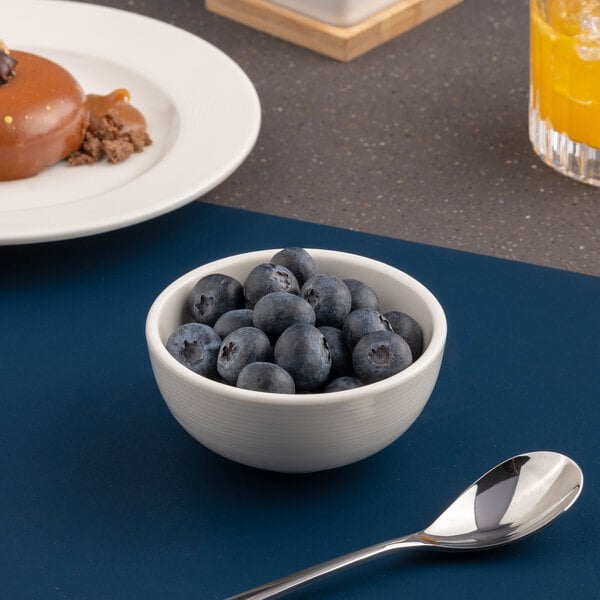 A small white embossed porcelain bowl filled with blueberries.
