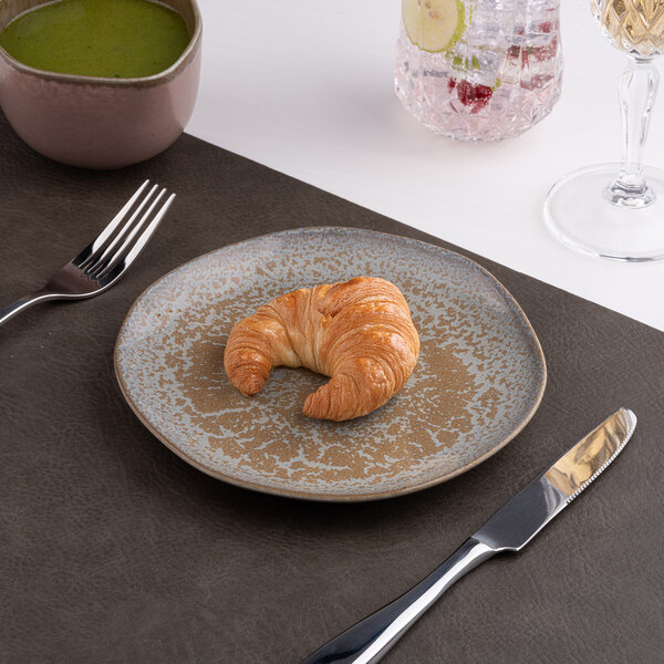 A gold and brown irregular round porcelain flat plate with a croissant on it.