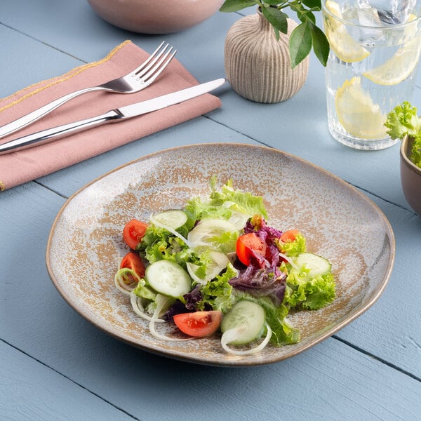 A gold and brown irregular round porcelain deep plate with a salad served on it.