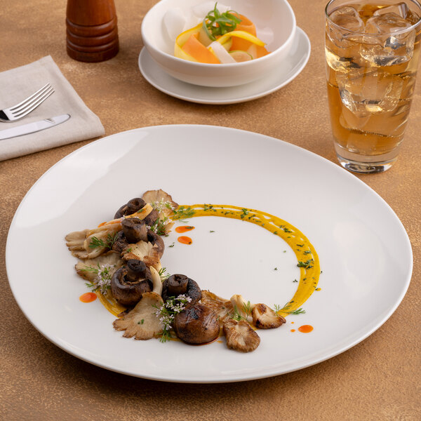 A large, round, warm white porcelain coupe plate with a slanted edge, featuring a gourmet mushroom dish artfully plated.
