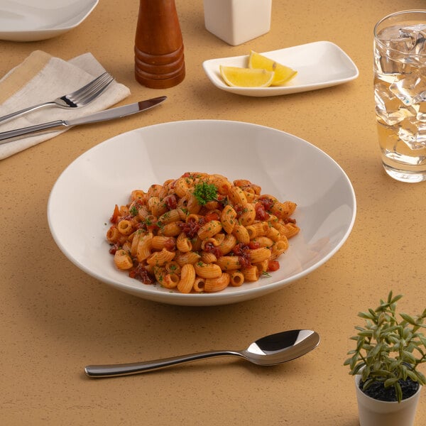 A round, warm white porcelain coupe deep plate filled with pasta, displayed on a table setting.