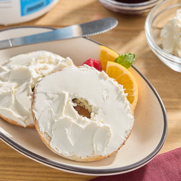 A sliced bagel with cream cheese spread on a plate, garnished with orange slices and a raspberry.