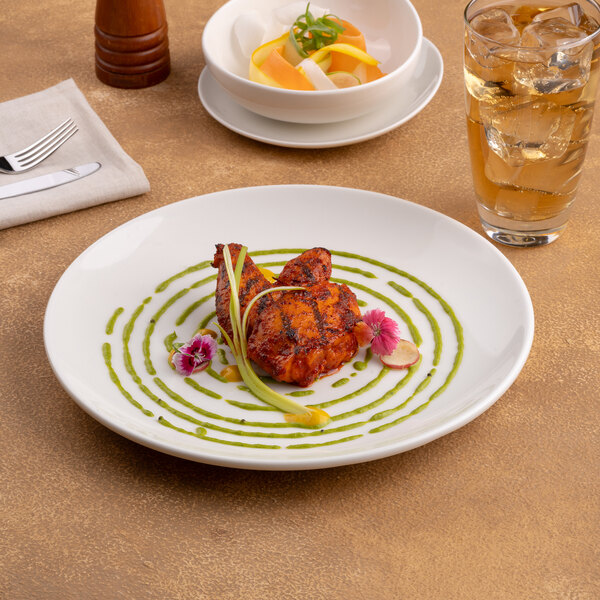 A round, warm white porcelain rimless coupe plate with a modern design, shown with a plated dish.