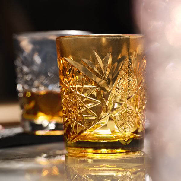 A 12 oz. topaz-colored rocks glass with an intricate cut-glass pattern.