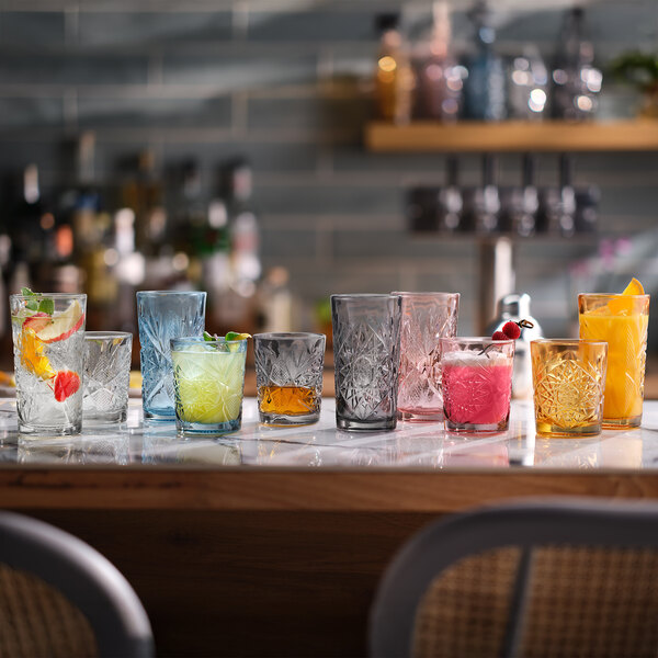 A clear, intricately patterned 12 oz. rocks glass from the Libbey Hobstar collection, shown with colorful drinks and garnishes.