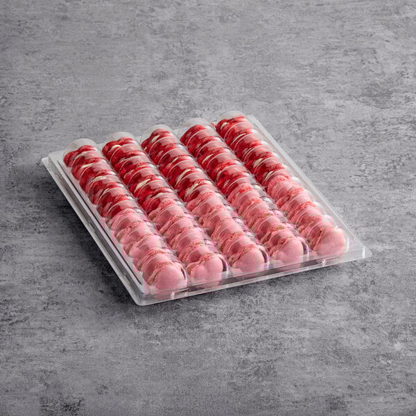 A plastic tray containing rows of pink heart-shaped macarons.