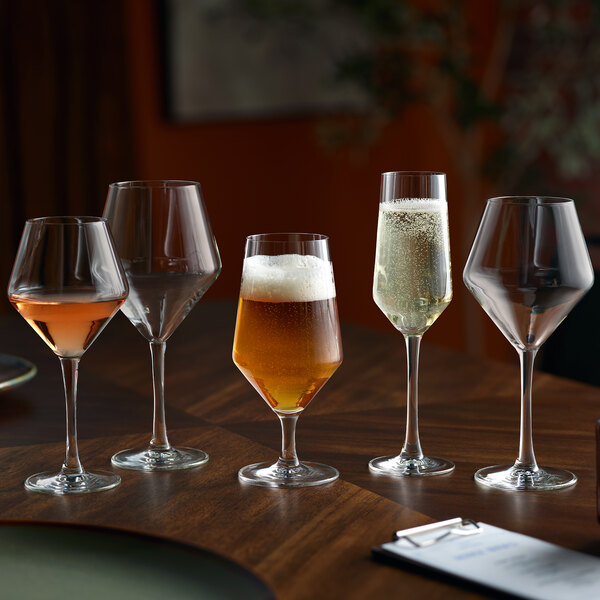 A set of five assorted stemmed glasses, including a diamond-shaped flute glass, displayed on a wooden table.