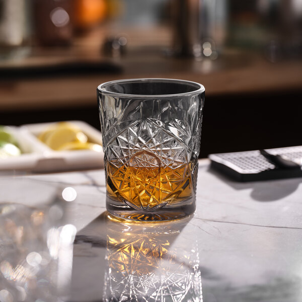 A graphite-colored, intricately patterned rocks glass partially filled with a brown liquid.