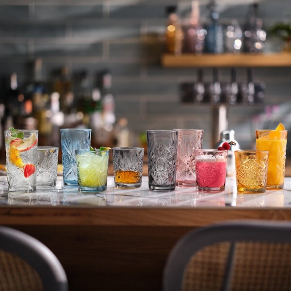 A set of colored Libbey Hobstar 16 oz. sapphire cooler glasses displayed on a bar counter, each filled with different beverages and garnishes.