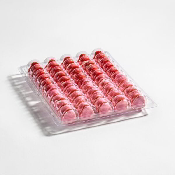 A clear plastic tray containing 50 heart-shaped pink macarons arranged in rows.