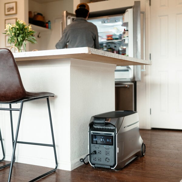 A portable lithium-ion power station positioned on the floor near a kitchen island.