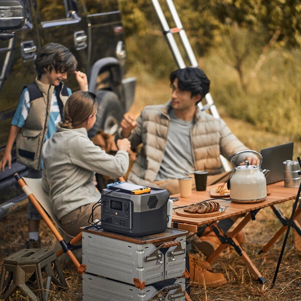 A portable lithium-ion power station placed on a stack of metal cases at a campsite.