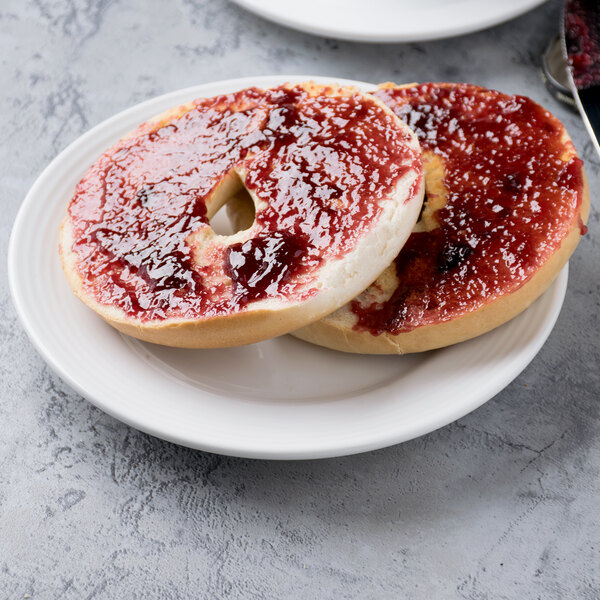 A white porcelain plate holding a sliced bagel with jam spread on top.