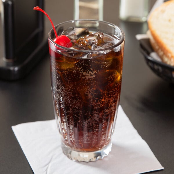 A 12 oz. Libbey Winchester beverage glass filled with a dark soda, ice, and garnished with a cherry, placed on a white napkin.