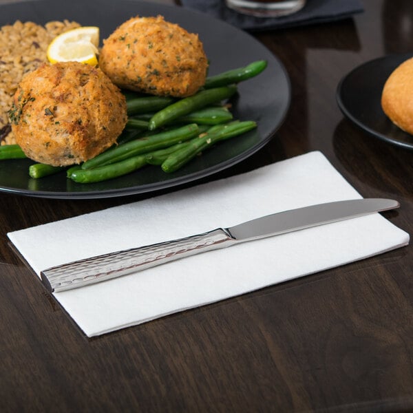 A stainless steel dinner knife with a textured handle placed on a white napkin.