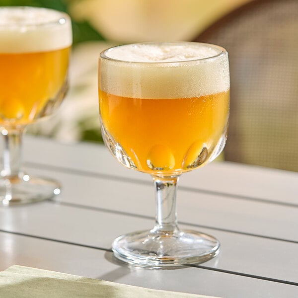 A clear glass schooner with a short stem, filled with a frothy, golden beverage.