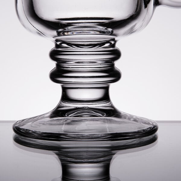 A clear glass coffee mug with a decorative, sturdy pedestal base.