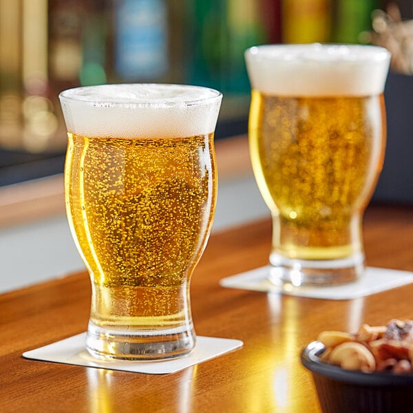 A pair of Libbey 16.75 oz. stackable craft beer glasses filled with beer, placed on coasters on a wooden surface.