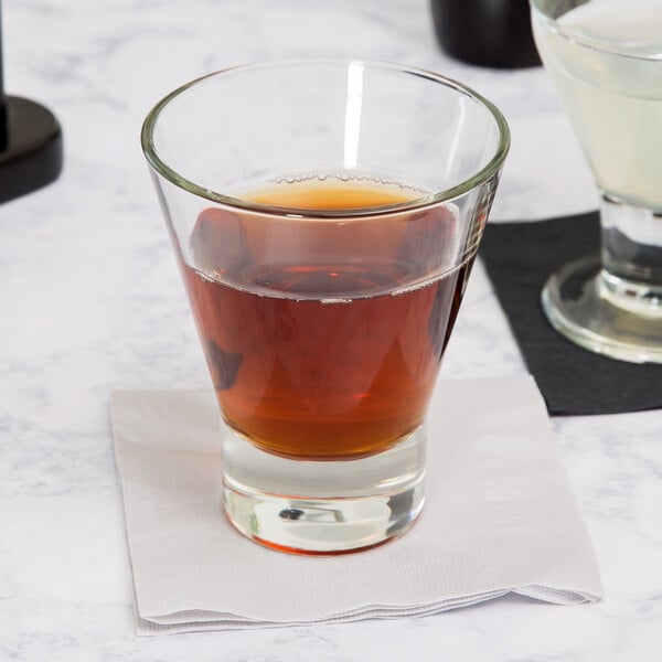 A clear Libbey Series V 11.8 oz. rocks glass filled with a brown liquid, placed on a white napkin.