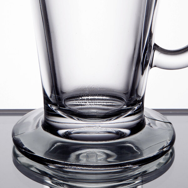 A clear glass coffee mug with a handle and a thick, round base.