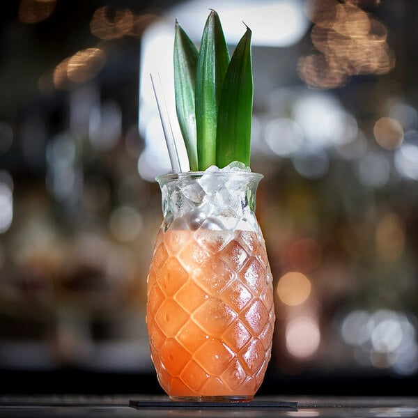 A 17 oz. pineapple-shaped glass filled with a tropical drink, garnished with pineapple leaves and served with straws.