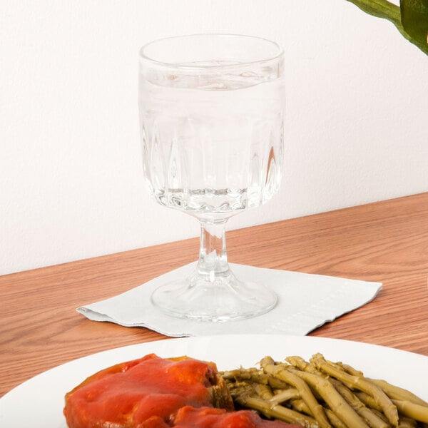 A clear glass goblet filled with water, placed on a white napkin next to a plate of food on a wooden table.