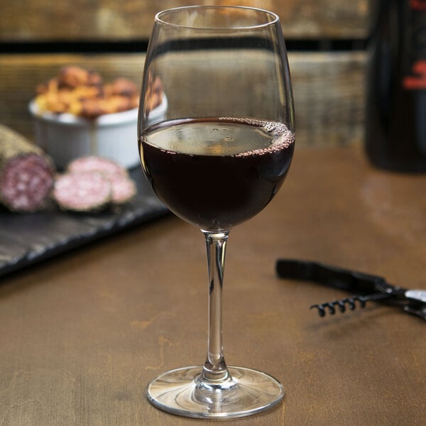 A clear wine glass partially filled with red wine, placed on a wooden surface.