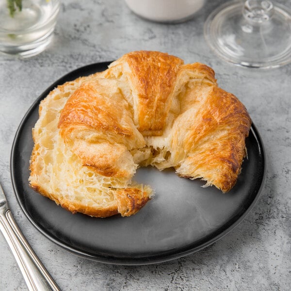 A black porcelain plate with a croissant on it.