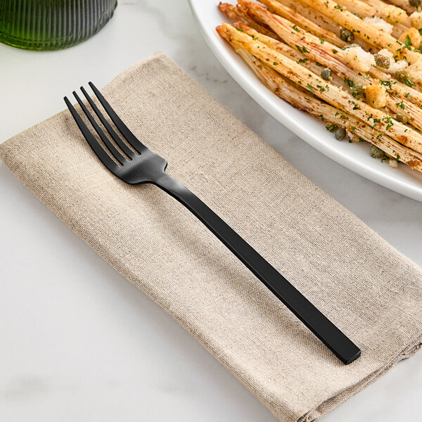 A black satin stainless steel dinner fork placed on a beige napkin.