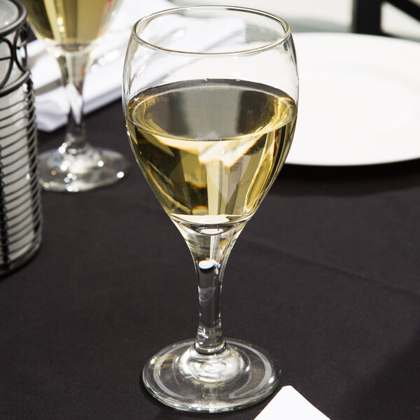 A clear glass goblet filled with white wine on a black tablecloth.