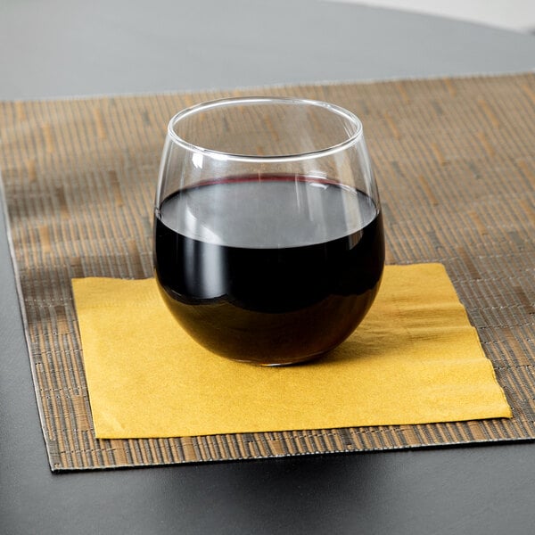 A clear stemless wine glass filled with red wine, placed on a yellow napkin.