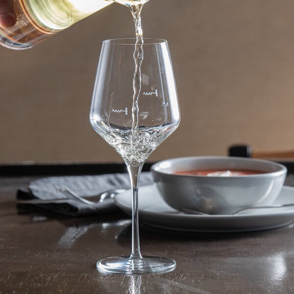 A clear stemmed wine glass with pour control markings being filled with white wine.