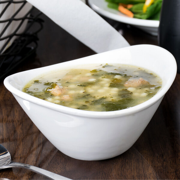 A small, bright white oval porcelain bowl filled with soup.