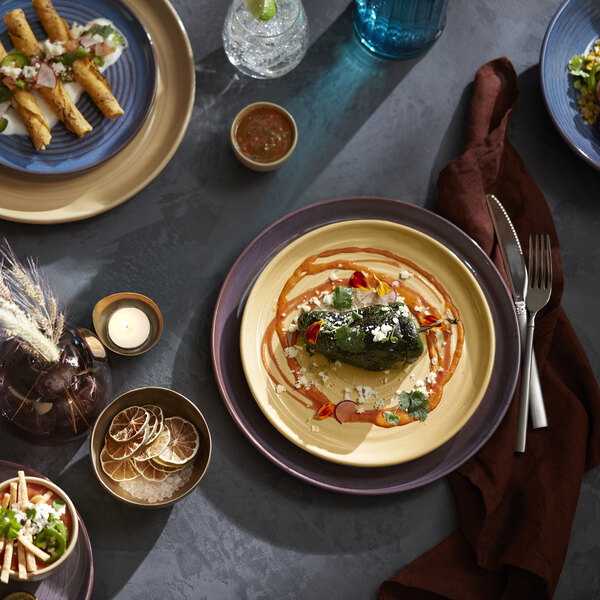 An 11 1/8 inch tan terracotta stack plate from the Libbey Canyonlands collection, shown with a plated dish and surrounded by other tableware.