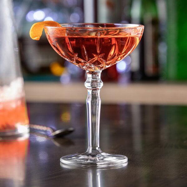 A clear Nachtmann Noblesse 6.25 oz. cocktail glass filled with a reddish drink and garnished with an orange twist.