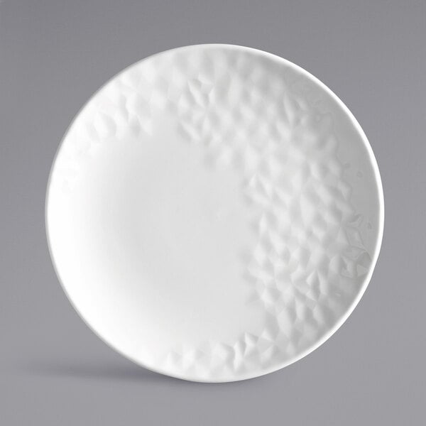 A white porcelain round coupe plate with a textured geometric pattern on one side.