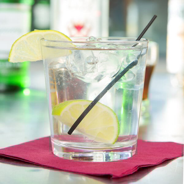 A clear 12 oz. rocks glass filled with ice, garnished with lime wedges, and placed on a red napkin.