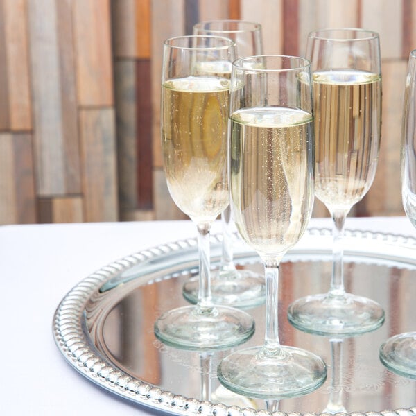 A set of Libbey Bristol Valley 6 oz. flute glasses filled with sparkling wine on a silver tray.