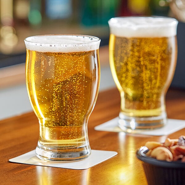 A 14.25 oz. stackable craft beer glass filled with beer, placed on a coaster on a wooden surface.
