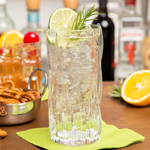 A clear Nachtmann Shu Fa 12.25 oz. longdrink or Collins glass filled with ice and garnished with lime and rosemary, placed on a green napkin.