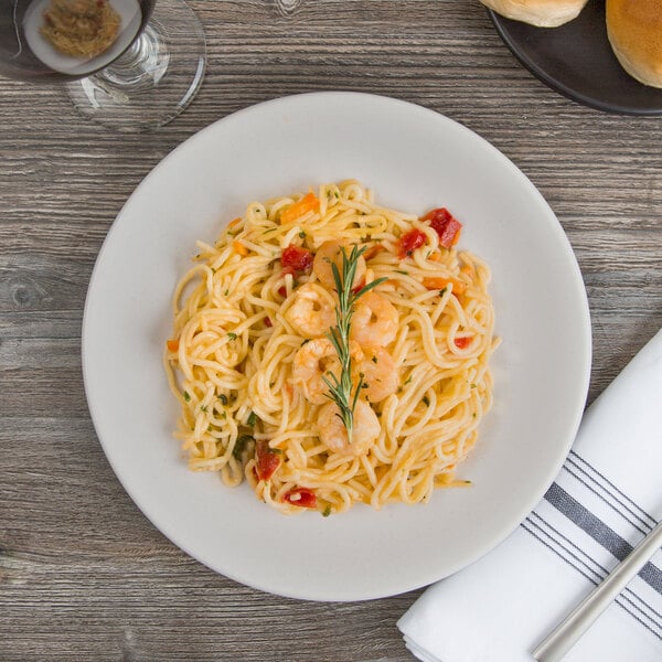 A white porcelain coupe plate with a serving of shrimp pasta, garnished with herbs.